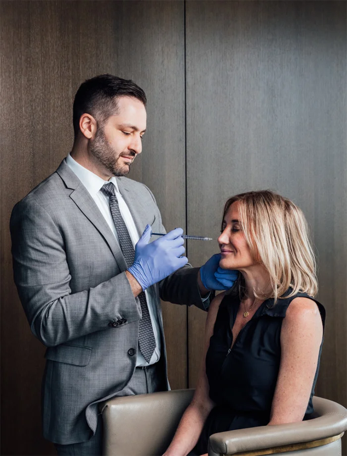 Dr James Economides in suit examining female patient's face for cosmetic consultation - Botox in Chevy Chase, MD
