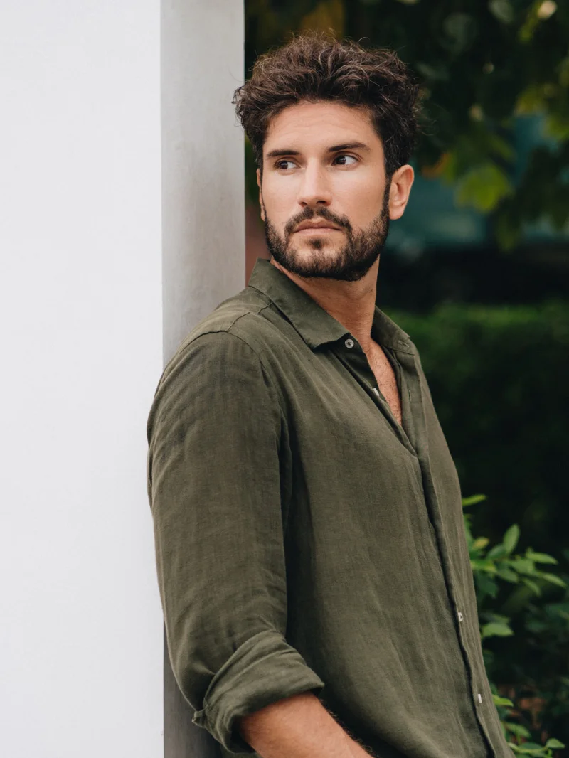 Handsome bearded man in olive green shirt leaning against white wall outdoors with natural background - Male gynecomastia in Chevy Chase, MD