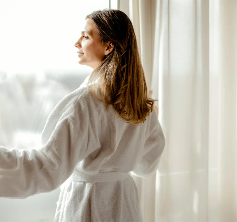 Woman in white robe looking out window with natural light in modern medical office setting - in Chevy Chase, MD