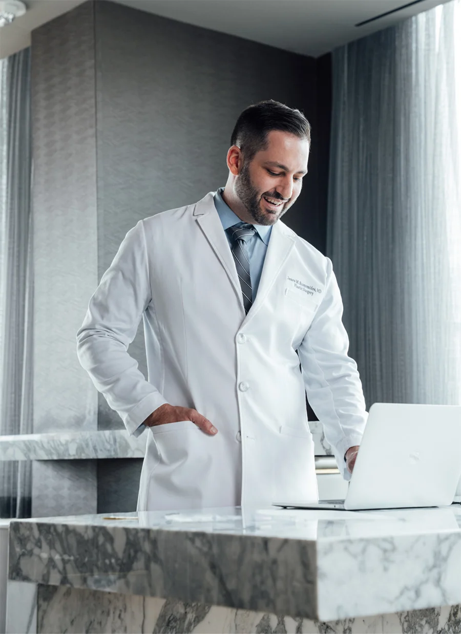 Doctor James Economides in white coat reviewing medical information on laptop at modern clinic desk - in Chevy Chase, MD