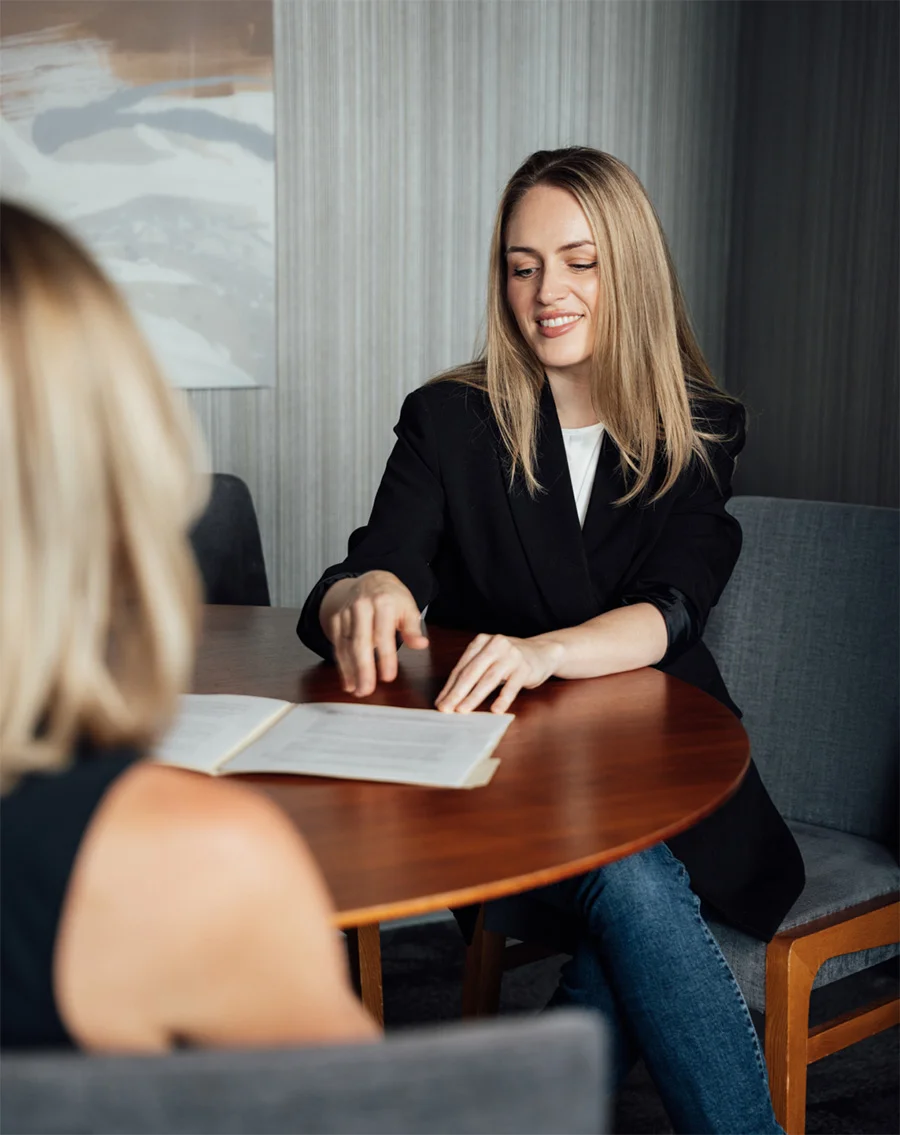 Professional woman in black blazer discussing documents with client across wooden table in office setting - in Chevy Chase, MD