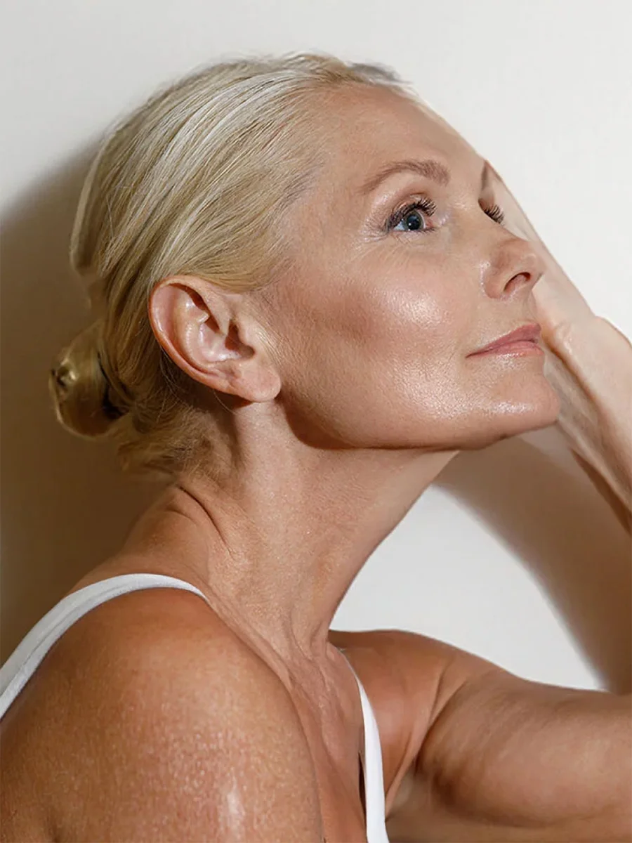 Mature woman with blonde hair in white tank top touching face, contemplating cosmetic procedure - in Chevy Chase, MD