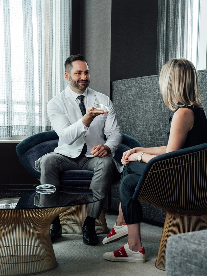 Dr James Economides in white shirt meeting with female client in modern office setting - Breast augmentation in Chevy Chase, MD