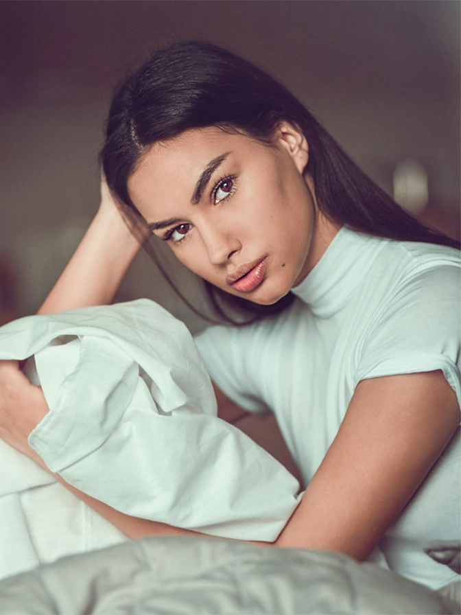 Woman in light blue dress posing elegantly with hand near face in soft-focus portrait photography - Buccal fat removal in Chevy Chase, MD