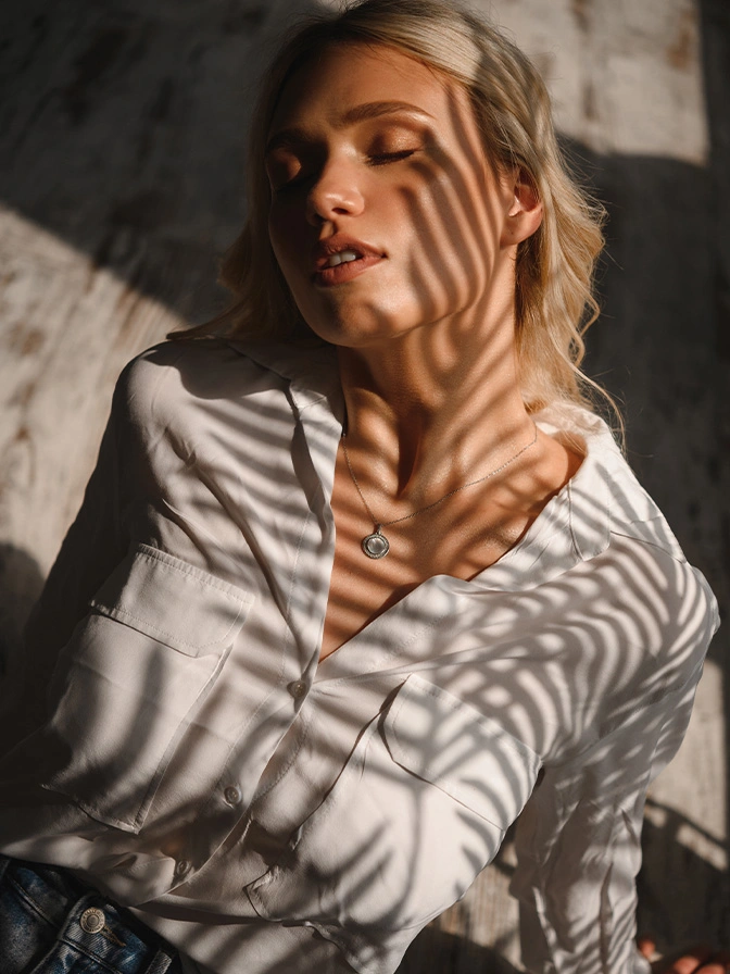 Woman in striped sweater with shadow patterns on face relaxing in natural sunlight - Chin augmentation in Chevy Chase, MD