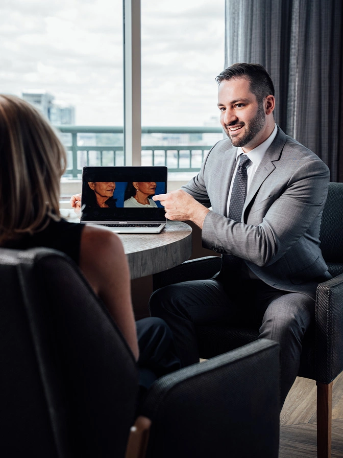 Dr James Economides in gray suit meeting with client in modern office setting with laptop - Deep neck lift in Chevy Chase, MD