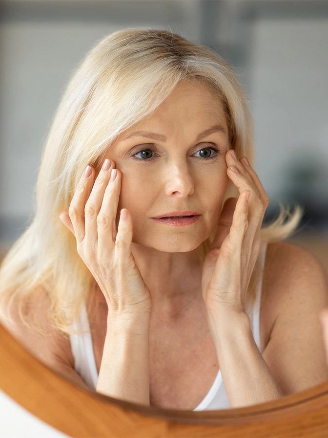 Mature woman with blonde hair touching face examining skin for anti-aging skincare routine - Fraxel dual in Chevy Chase, MD