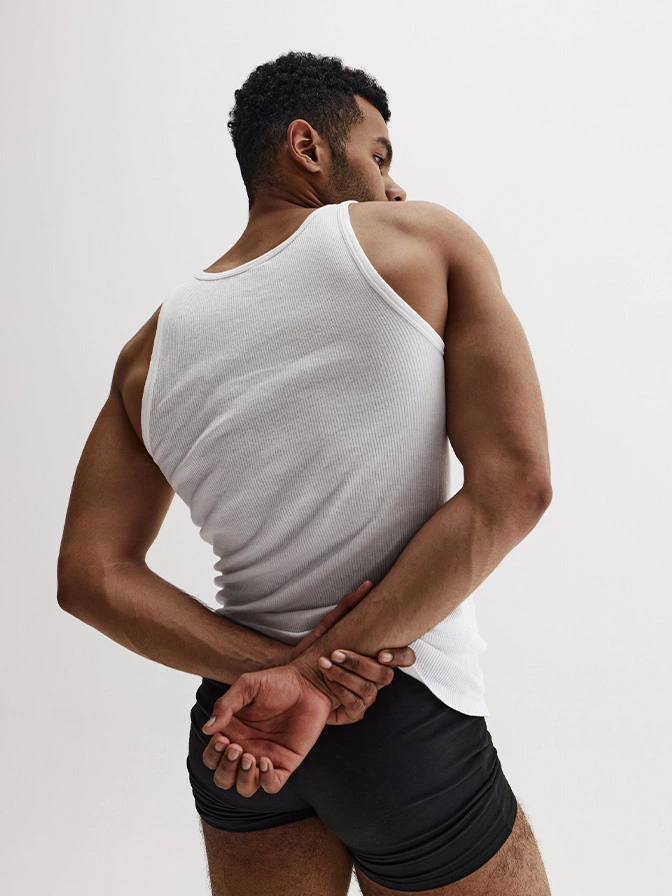 Athletic man in white tank top and black shorts stretching his back and shoulders, rear view pose - Male buttock augmentation in Chevy Chase, MD