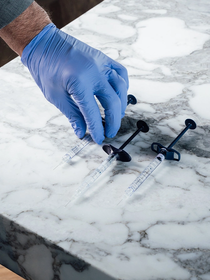 Hand in blue glove placing cabinet hardware pulls on white marble countertop for installation - Non surgical rhinoplasty in Chevy Chase, MD