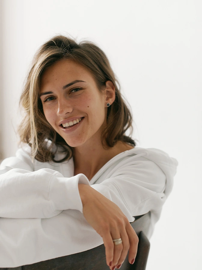 Smiling woman in white shirt with arms crossed looking at camera in bright natural light - otoplasty in Chevy Chase, MD