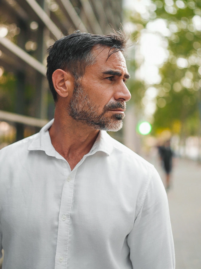 Professional man with beard in white shirt looking away outdoors in urban setting - PRP hair restoration in Chevy Chase, MD