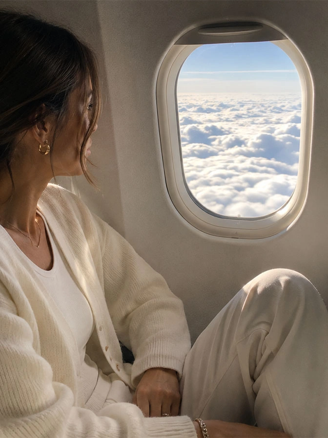 Woman in white outfit looking out airplane window at clouds during flight for medical travel - in Chevy Chase, MD